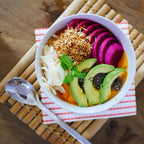 Bunte Smoothie Bowl mit Avocado, Drachenfrucht, Kokoschips und Minze auf Bambusmatte