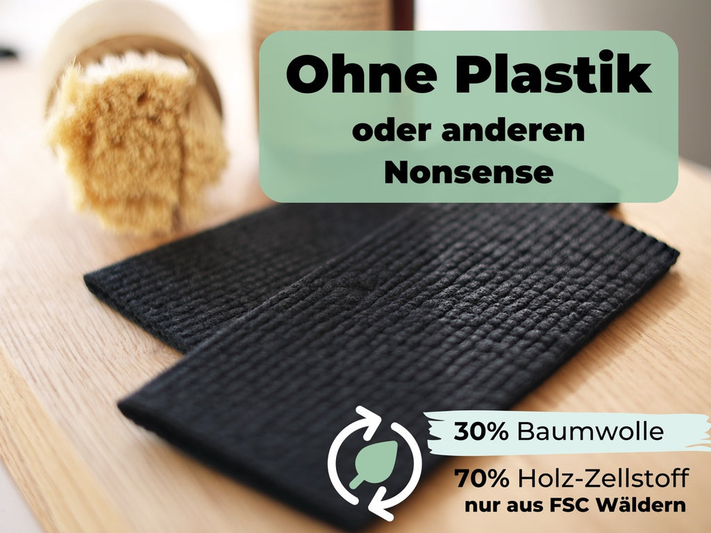 schwarze Küchentücher aus Baumwolle und Holz-Zellstoff auf Holztisch mit Naturbürste im Hintergrund
